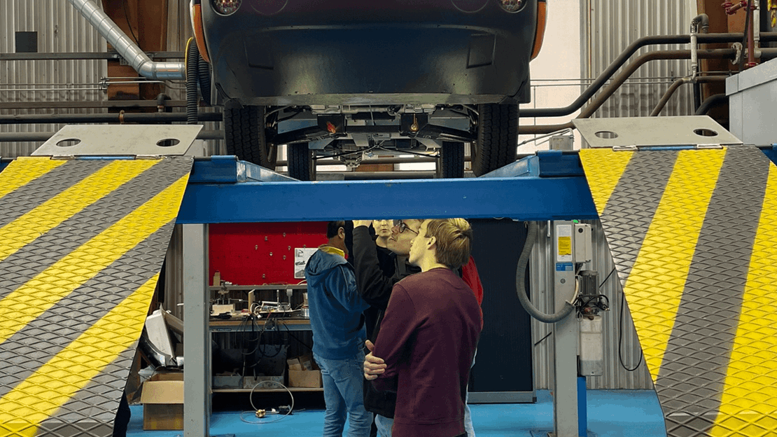Eerstejaars Automotive studenten bekijken de onderkant van een licht elektrisch vrachtvoertuig (Spijkstaal)
